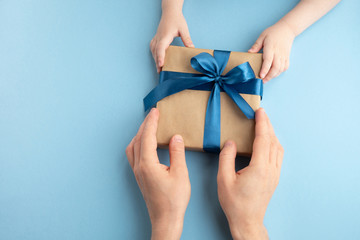 Fathers day, birthday and holiday concept. Little child gives his father gift on light blue background. Top view, flat lay, copy space