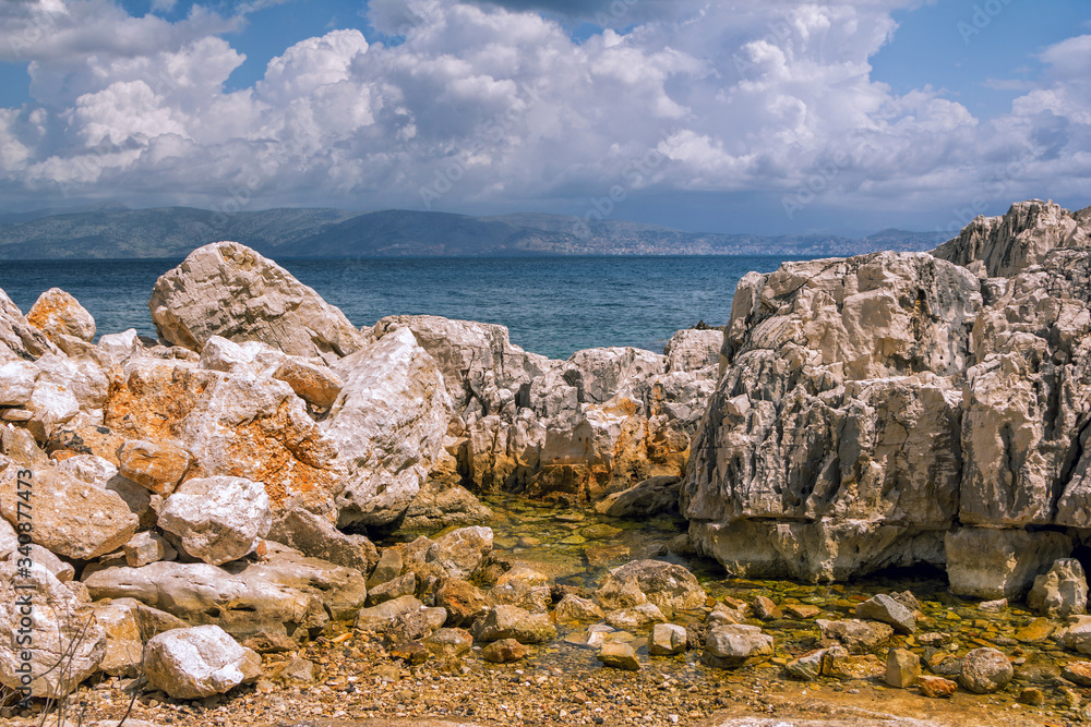 Beautiful landscape with sea bay, rocks and cliffs, blue sky and mountains on the horizon. Corfu Island, Greece. 