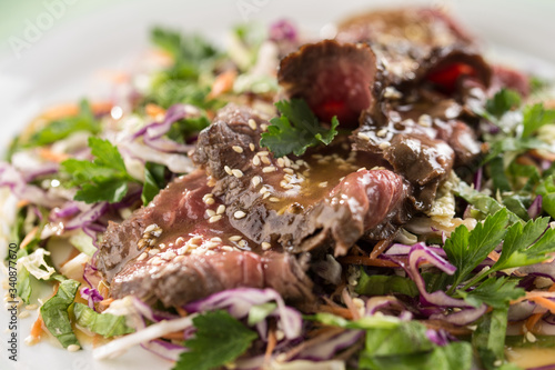 Asian cabbage salad with roast beef and sesame seeds on wooden table