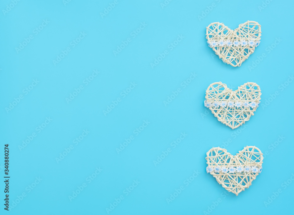 White rattan hearts with ribbon with flowers on blue background.  Mother’s day, Valentine’s day, Wedding, Birthday or other suitable event celebration card concept. Flat lay with copy space for text.