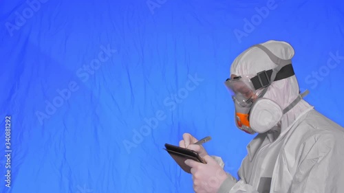 Scientist virologist in respirator makes write in an tablet computer with stylus. Man wearing protective medical mask. Concept health safety virus coronavirus epidemic 2019 nCoV. Chroma key blue. photo