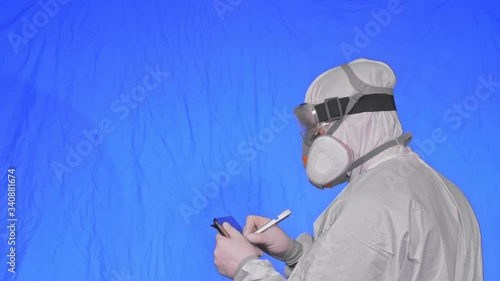 Scientist virologist in respirator makes write in an tablet computer with stylus. Man wearing protective medical mask. Concept health safety virus coronavirus epidemic 2019 nCoV. Chroma key blue. photo