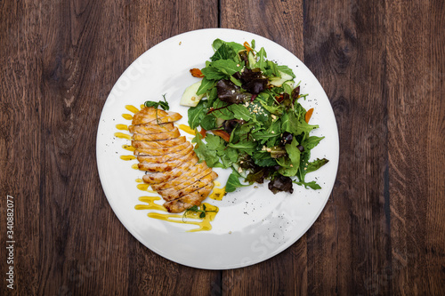 Grilled chicken breast and salad with lettuce and cherry tomatoes in mustard sauce on a plate on a wooden table. photo