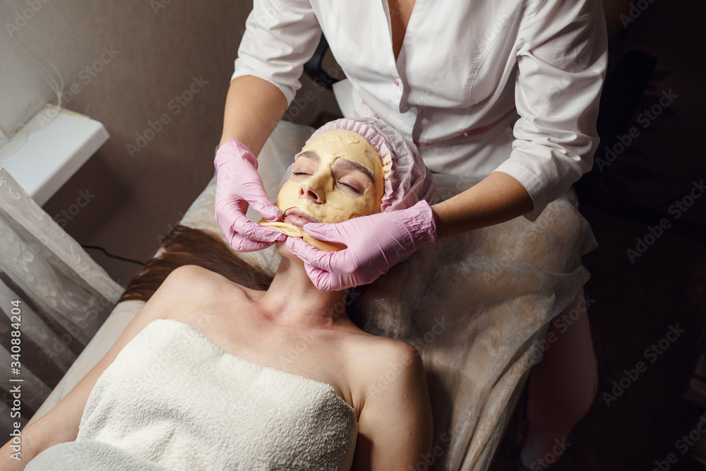 cosmetology specialist applying gold facial mask using brush
