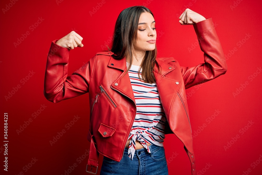 Young beautiful brunette woman wearing casual jacket standing over red background showing arms muscles smiling proud. Fitness concept. Young beautiful brunette woman wearing casual jacket standing over red background showing arms muscles smiling proud. Fitness concept.
