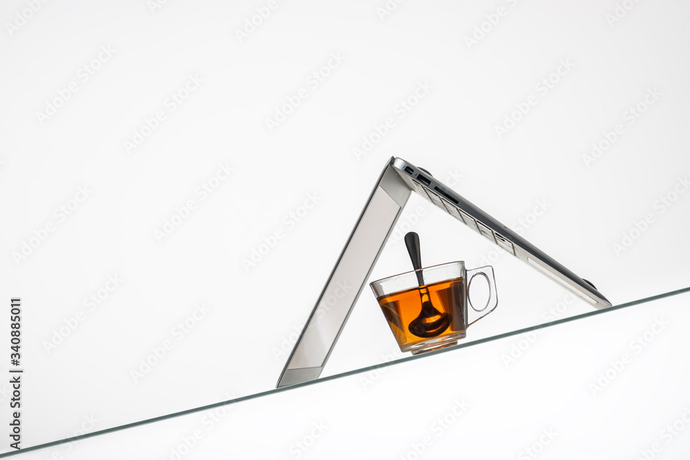 cup with hot herbal tea and laptop on inclined glass table surface cup with hot herbal tea and laptop on inclined glass table surface