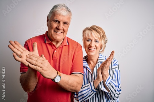 Senior beautiful couple standing together over isolated white background clapping and applauding happy and joyful, smiling proud hands together