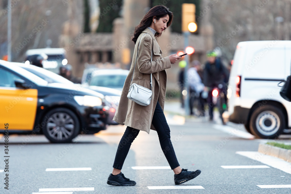 Pretty young woman crossing the street while listen to music with the wireless earphones.