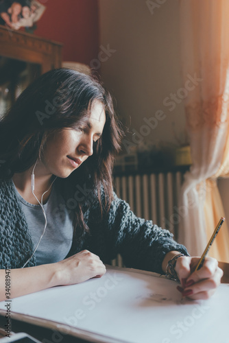 Young beautiful middle eastern woman indoor at home drawing on paper listening music photo