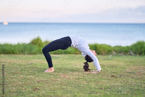 Young beautiful sportwoman practicing yoga. Coach teaching wheel pose at park
