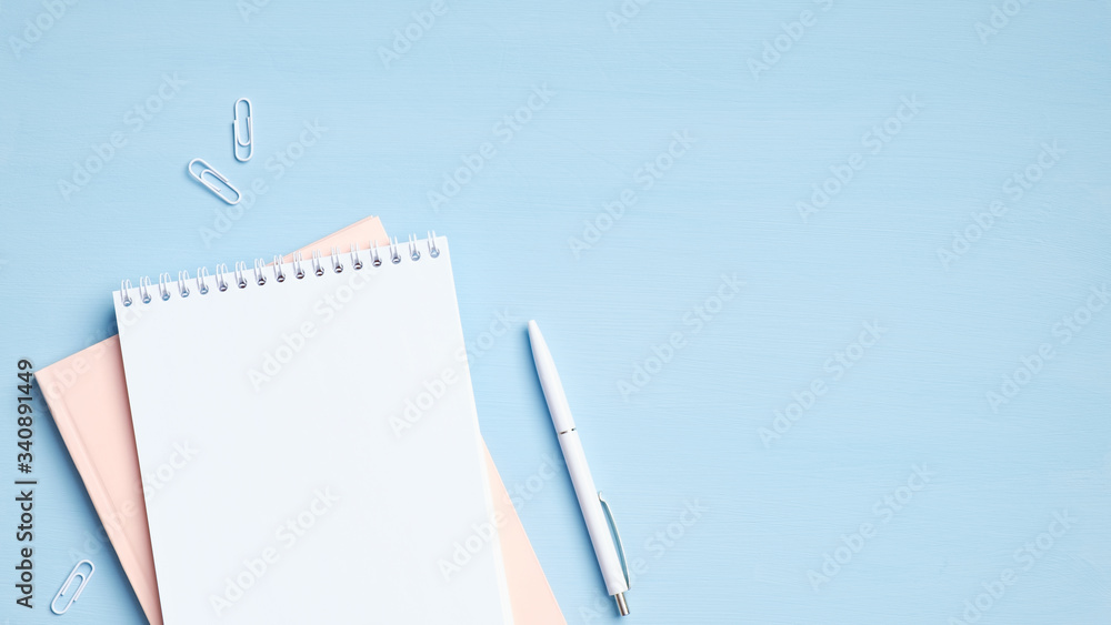 Notepad and pen on blue background. Minimal style feminine workspace, business and education concept. Flat lay, top view, copy space Notepad and pen on blue background. Minimal style feminine workspace, business and education concept. Flat lay, top view, copy space