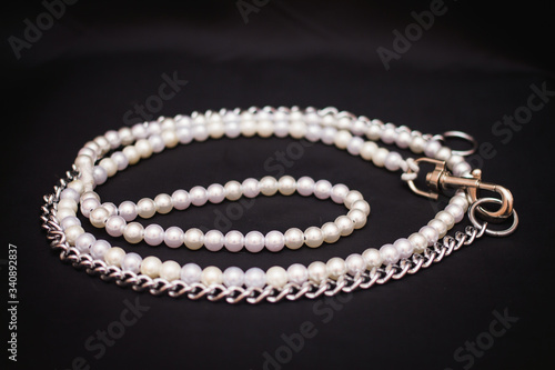Beautiful ring made of white and beige pearls. Leash for a dog on a black background.