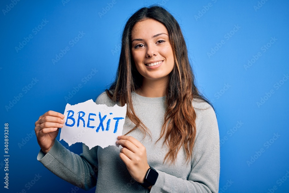 Young beautiful brunette woman holding paper with brexit message over blue background with a happy face standing and smiling with a confident smile showing teeth Young beautiful brunette woman holding paper with brexit message over blue background with a happy face standing and smiling with a confident smile showing teeth