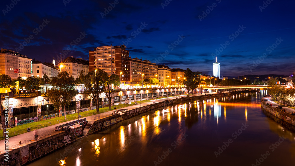 A view along the Danube Canal during the blue hour. People buildings and bars can be seen.