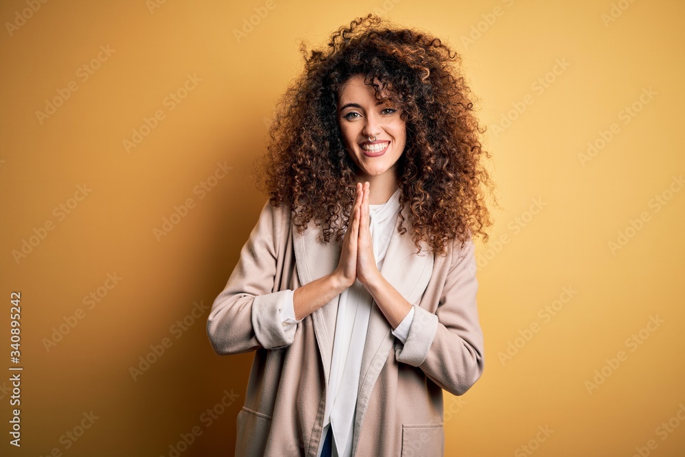 Young beautiful brunette woman with curly hair and piercing wearing casual t-shirt and diadem praying with hands together asking for forgiveness smiling confident. Young beautiful brunette woman with curly hair and piercing wearing casual t-shirt and diadem praying with hands together asking for forgiveness smiling confident.