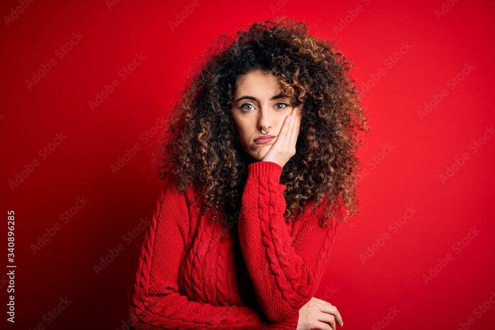 Young beautiful woman with curly hair and piercing wearing casual red sweater thinking looking tired and bored with depression problems with crossed arms. Young beautiful woman with curly hair and piercing wearing casual red sweater thinking looking tired and bored with depression problems with crossed arms.