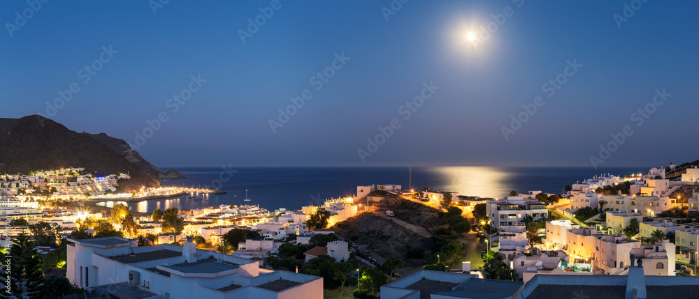 Panoramic night view of the city of San José in the Cabo de Gata Natural Park, Almeria, with the Mediterranean sea in the background and the reflection of the moon.