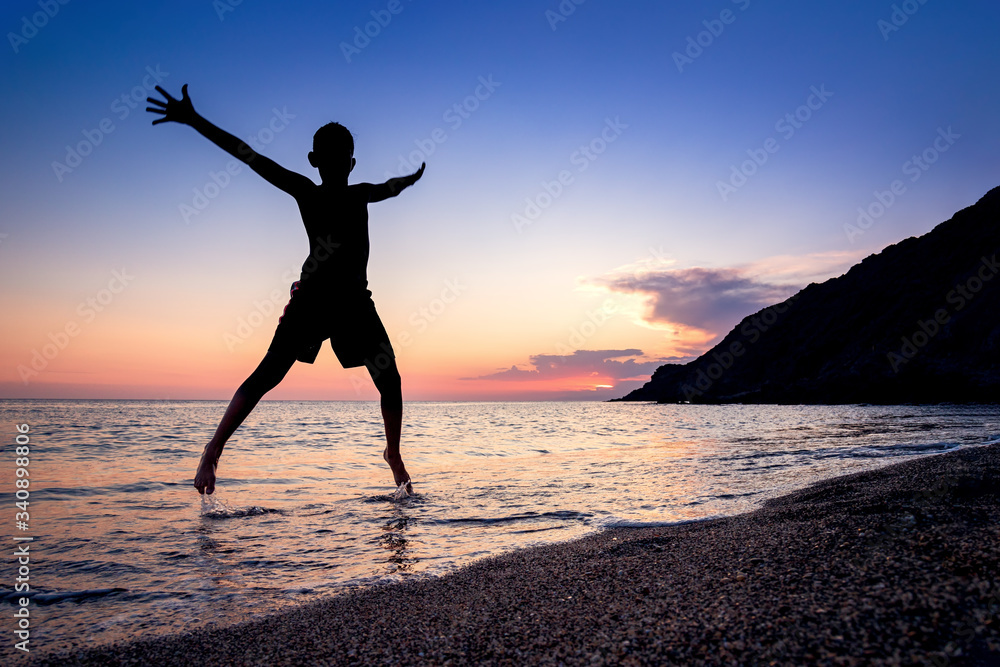 Backlit boy silhouette jumping with joy over the water on a beach of Cabo de Gata Natural Park, Almeria.