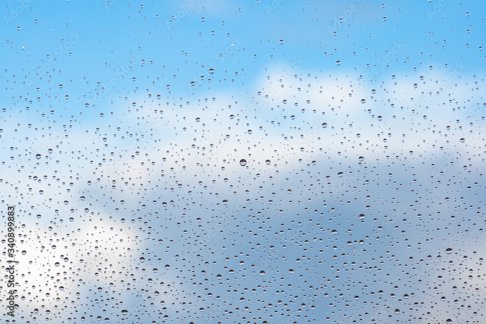 Water drops on the glass of a window with a blue sky and clouds in the background Water drops on the glass of a window with a blue sky and clouds in the background