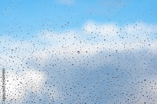 Water drops on the glass of a window with a blue sky and clouds in the background