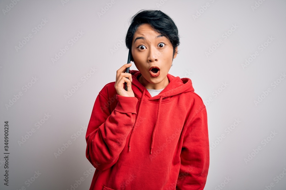 Young beautiful asian girl having conversation talking on the smartphone over white background scared in shock with a surprise face, afraid and excited with fear expression Young beautiful asian girl having conversation talking on the smartphone over white background scared in shock with a surprise face, afraid and excited with fear expression
