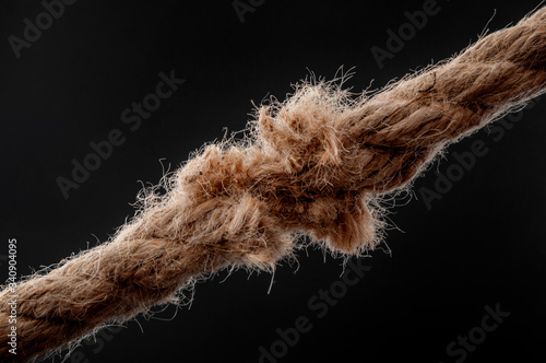 Weakness, vulnerability and single point of failure concept with worn rope string  breaking under physical stress pulling on it isolated on black background photo