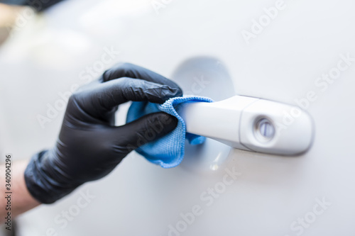 Man hand wearing protective glove and using small microfiber cloth to eliminate dirt or bacteria from car door handle.