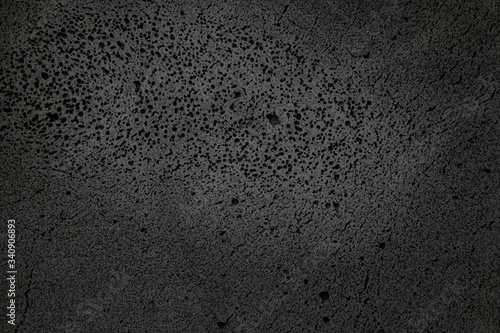 coarse-textured black background with many holes in basalt material. © J. studio