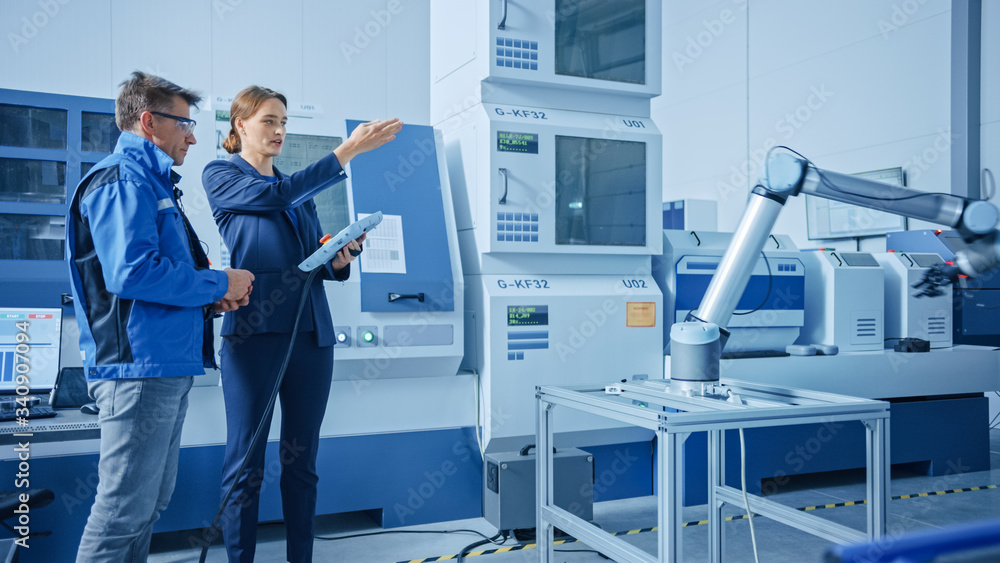 Modern Factory: Female Project Manager and Male Engineer Standing, Talking and Using Tablet Computer for Programming Robot Arm Assembly Line. Contemporary Facility with High Tech CNC. Indsutry 4.0 Modern Factory: Female Project Manager and Male Engineer Standing, Talking and Using Tablet Computer for Programming Robot Arm Assembly Line. Contemporary Facility with High Tech CNC. Indsutry 4.0