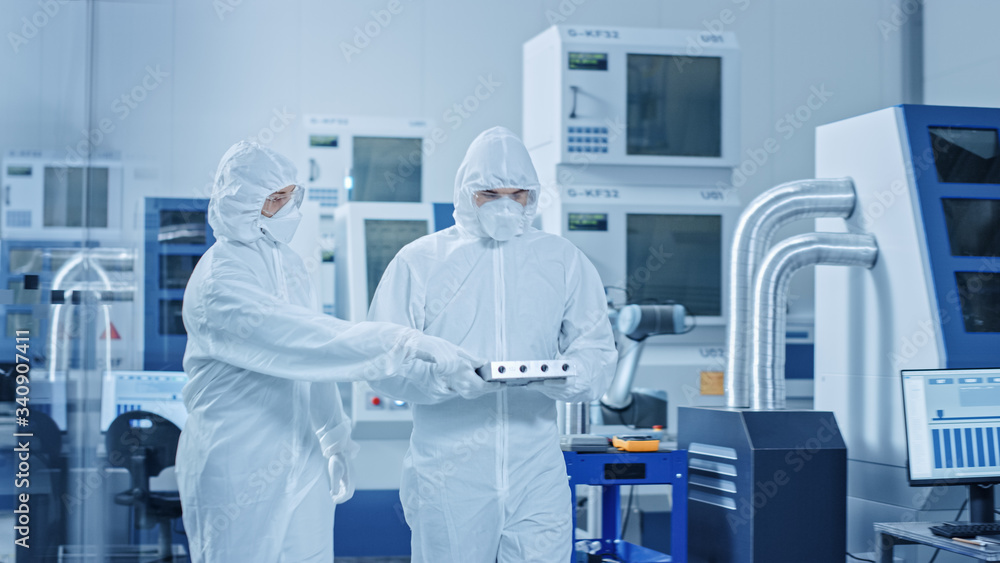 Naklejka premium Sterile Modern Factory: Professionals in Coveralls, Masks Walk Through Workshop and Talk. Medical Electronics Manufacturing Laboratory with High Tech CNC Machinery, Robot Arm Production Line.