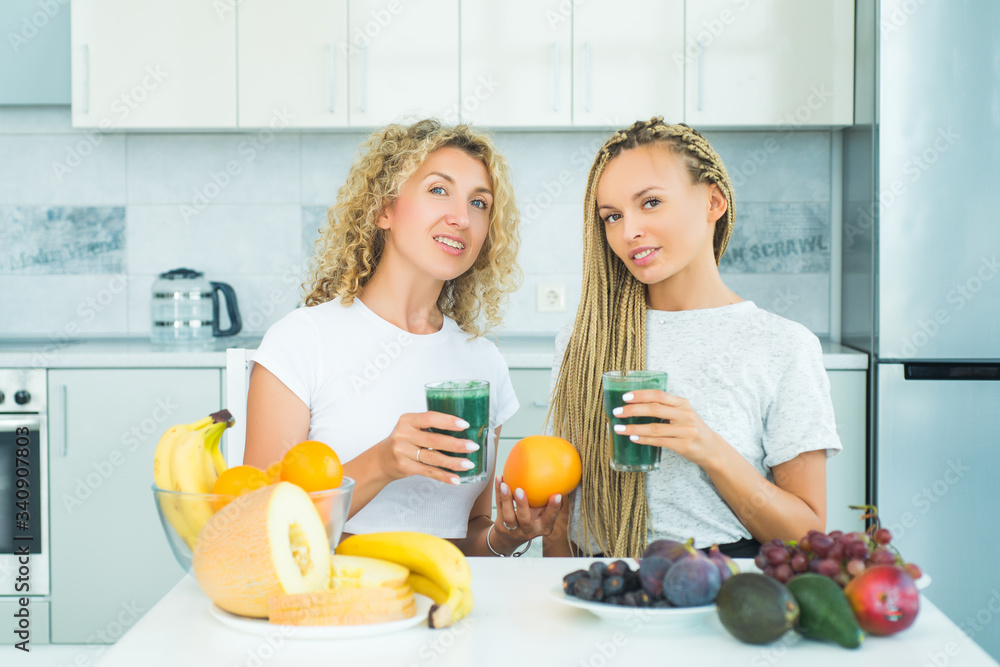 Two blonde healthy girls friends drinks green smoothie. Fitness and dieting. Food supplements. Weight loss. Glass is filled with fresh and useful smoothie made from spicy juicy vegetables and fruits. Two blonde healthy girls friends drinks green smoothie. Fitness and dieting. Food supplements. Weight loss. Glass is filled with fresh and useful smoothie made from spicy juicy vegetables and fruits.