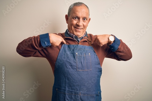 Senior handsome baker man wearing apron standing over isolated white background looking confident with smile on face, pointing oneself with fingers proud and happy.