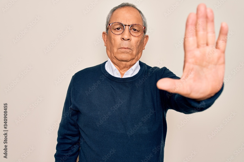 Senior handsome grey-haired man wearing sweater and glasses over isolated white background doing stop sing with palm of the hand. Warning expression with negative and serious gesture on the face. Senior handsome grey-haired man wearing sweater and glasses over isolated white background doing stop sing with palm of the hand. Warning expression with negative and serious gesture on the face.