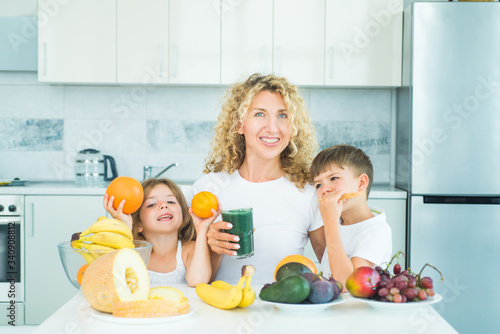Family mother and chilen daughter and son blended green and orange smoothie with healthy fruits ingredients. Summer ration. photo