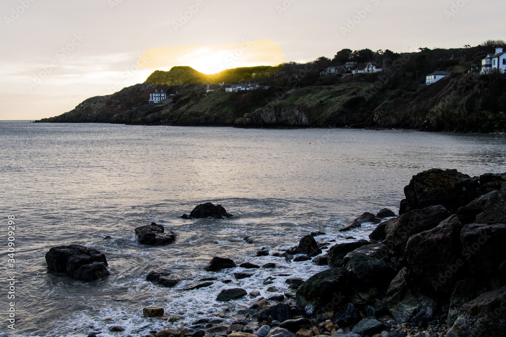 Beautiful sunset on irish coast. 
The waves hit the rocks on the shore creating white foam.