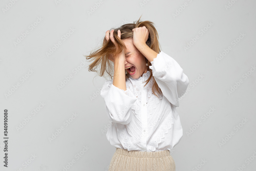Young woman with a headache holds her head isolated on a white gray background. woman is very suffering from pain Young woman with a headache holds her head isolated on a white gray background. woman is very suffering from pain