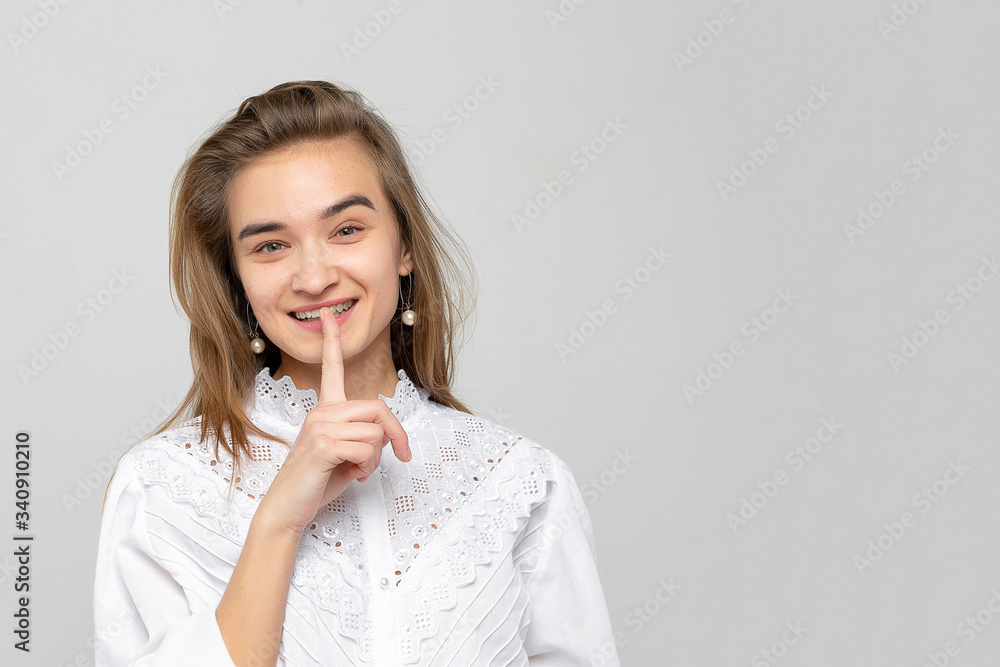 Portrait of a confident woman wears a white, shows a sign of silence, asks to keep information confidential, isolated on white-gray against a studio background. Secret gesture, shhh. Portrait of a confident woman wears a white, shows a sign of silence, asks to keep information confidential, isolated on white-gray against a studio background. Secret gesture, shhh.