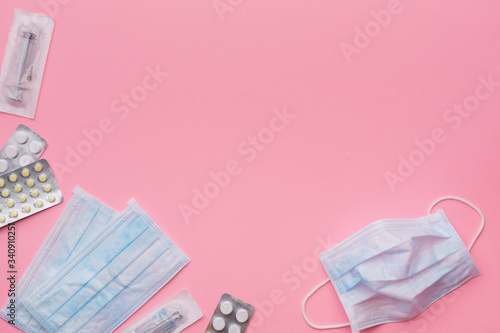 Medical protective masks, disposable syringe in sterile packaging and pharmaceutical packaging with pills on paper, pink bright background. The concept of protecting health from the virus. Copy space
