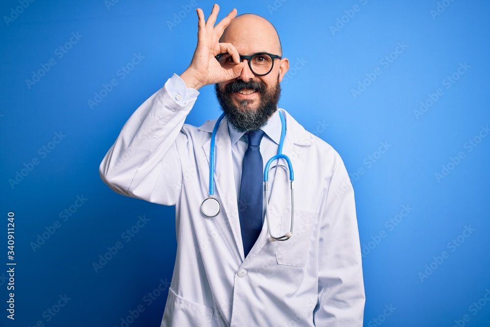 Handsome bald doctor man with beard wearing glasses and stethoscope over blue background doing ok gesture with hand smiling, eye looking through fingers with happy face. Handsome bald doctor man with beard wearing glasses and stethoscope over blue background doing ok gesture with hand smiling, eye looking through fingers with happy face.