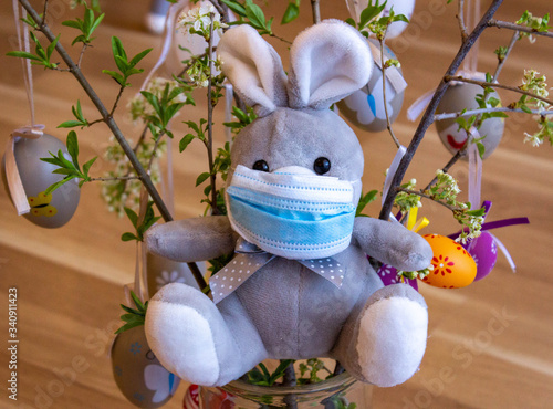 Easter Rabbit 2020 during Coronavirus COVID-19 worldwide pandemic with Easter bunny wearing a medical mask and a colorful egg tree.