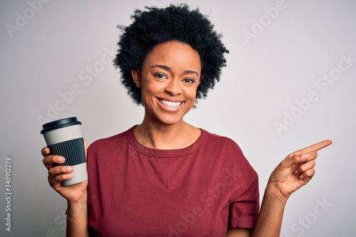 Young African American afro woman with curly hair drinking cup of coffee very happy pointing with hand and finger to the side
