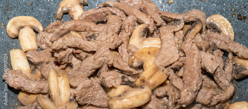 Homemade cooking veal and mushrooms in frying pan. Close-up macro photo of julian chopped meat. Smoke of meat cooked in its own juice comes out.