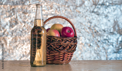 Basket with red fresh apples and a bottle of cider on a wooden table.