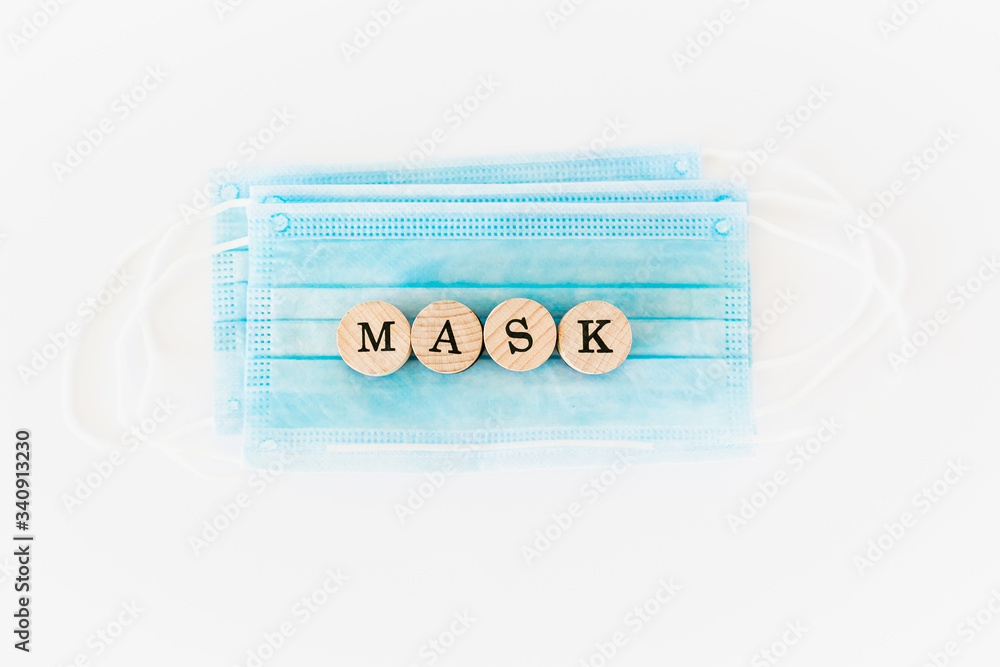 Word mask written with wooden blocks with black letters laying on protective surgical masks, flat lay concept Word mask written with wooden blocks with black letters laying on protective surgical masks, flat lay concept