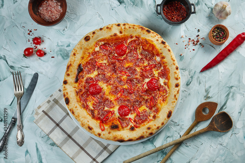 Freshly baked crispy pizza with hot pepper, salami, cheese and cherry tomatoes on a gray background in a composition with ingredients and kitchen utensils