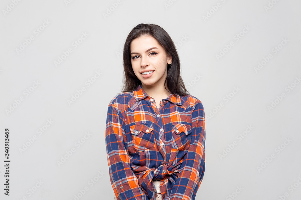 Beautiful young woman portrait. Portrait of a beautiful smiling brunette in a plaid shirt on a white-gray Beautiful young woman portrait. Portrait of a beautiful smiling brunette in a plaid shirt on a white-gray