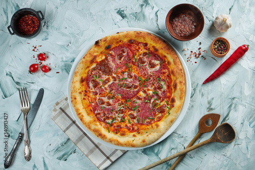 Freshly baked crispy pizza with salami and cheese on a gray background in a composition with ingredients and kitchen utensils