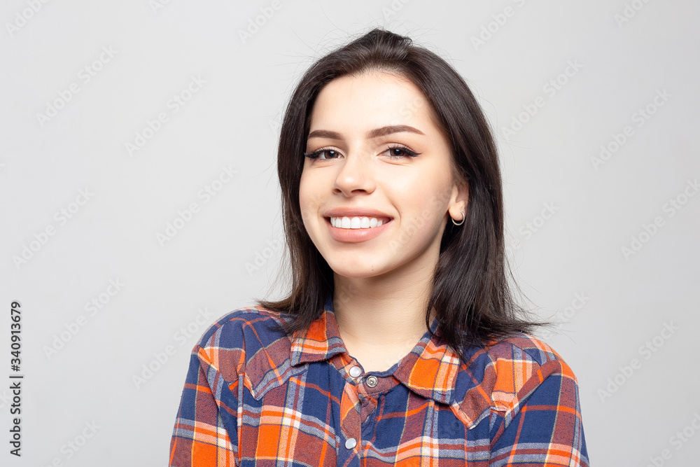 Beautiful young woman portrait. Portrait of a beautiful smiling brunette in a plaid shirt on a white-gray Beautiful young woman portrait. Portrait of a beautiful smiling brunette in a plaid shirt on a white-gray