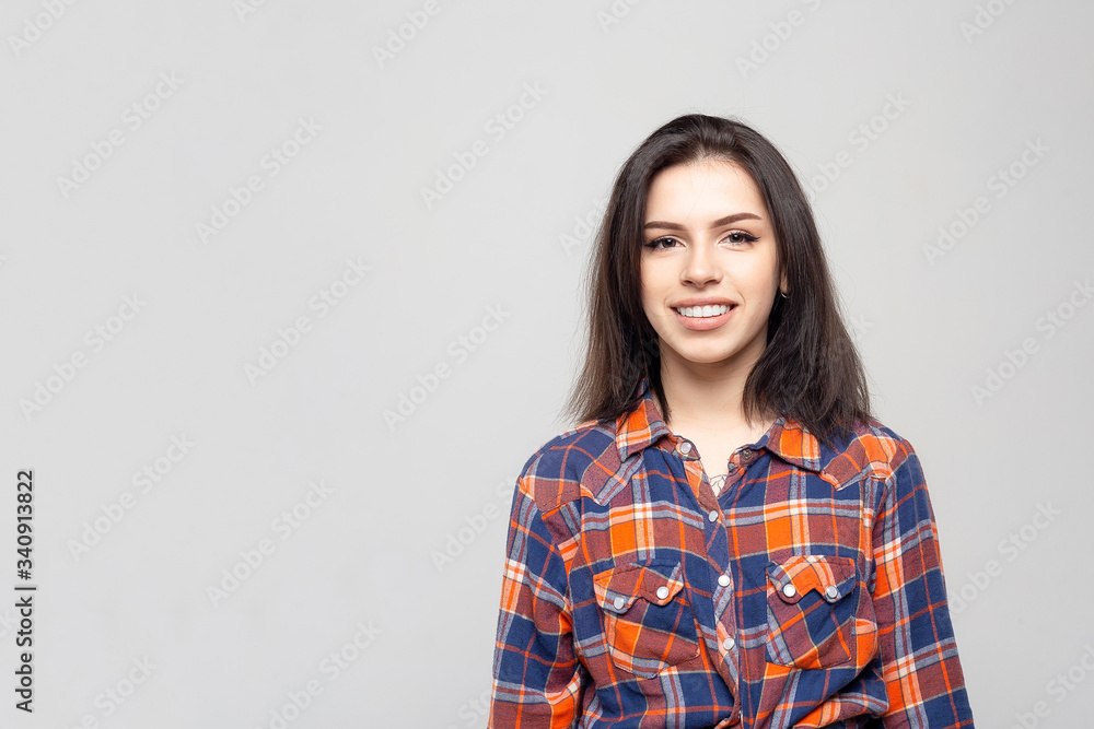 Beautiful young woman portrait. Portrait of a beautiful smiling brunette in a plaid shirt on a white-gray Beautiful young woman portrait. Portrait of a beautiful smiling brunette in a plaid shirt on a white-gray