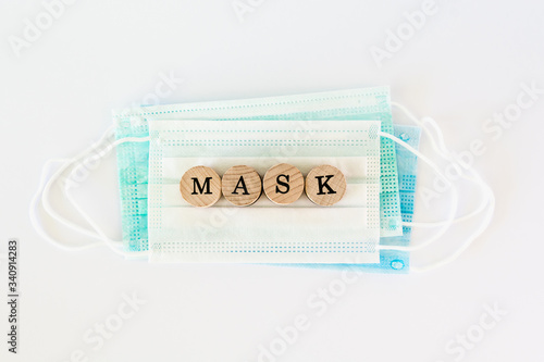 Word mask written with wooden blocks with black letters laying on protective surgical masks, flat lay concept